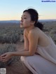 A woman in a pink dress sitting on a dirt road.