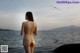 A woman in a gold bikini standing on a rock by the ocean.