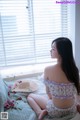 A woman sitting on a bed in front of a window.