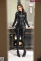 A woman in a black catsuit standing in front of a mirror.