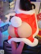 A woman in a santa claus outfit sitting on top of a suitcase.