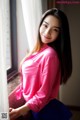 A woman in a pink shirt leaning against a window.