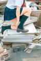 A woman in a school uniform sitting on top of a pile of books.