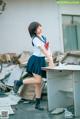 A woman in a school uniform standing next to a desk.