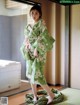 A woman in a green kimono standing on a tatami mat.