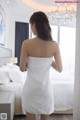 A woman in a white towel standing in front of a bed.