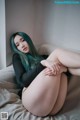 A woman with green hair sitting on a bed.