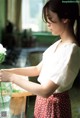 A woman in a white shirt and red skirt holding a vase of flowers.