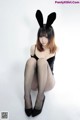 A woman in a black dress and bunny ears sitting on the ground.