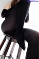 A woman in black tights sitting on a wooden chair.