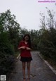 A woman in a red shirt and black skirt standing on a path.