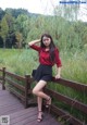 A woman in a red shirt and black skirt posing on a wooden bridge.