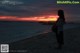 A woman standing on a beach looking at the sunset.