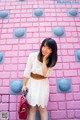 A woman standing in front of a pink brick wall.