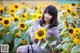 A woman sitting in a field of sunflowers holding a camera.