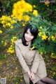 A woman sitting in front of a bush of yellow flowers.