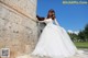 A woman in a wedding dress leaning against a stone wall.