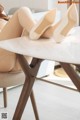 A woman sitting on top of a white table with her legs crossed.