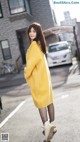 A woman in a yellow coat is standing on the street.