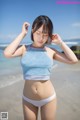 A woman in a blue top and white bikini standing on a beach.