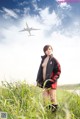 A woman standing in a field with an airplane in the background.