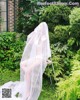 A woman in a white lingerie sitting on a chair in the grass.