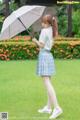 A woman standing in the grass holding an umbrella.