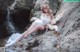 A woman in a white dress sitting on a rock next to a waterfall.