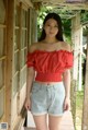 A woman in a red top and denim shorts posing for a picture.